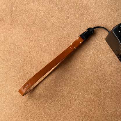 Brown leather strap with a black cord on a beige surface